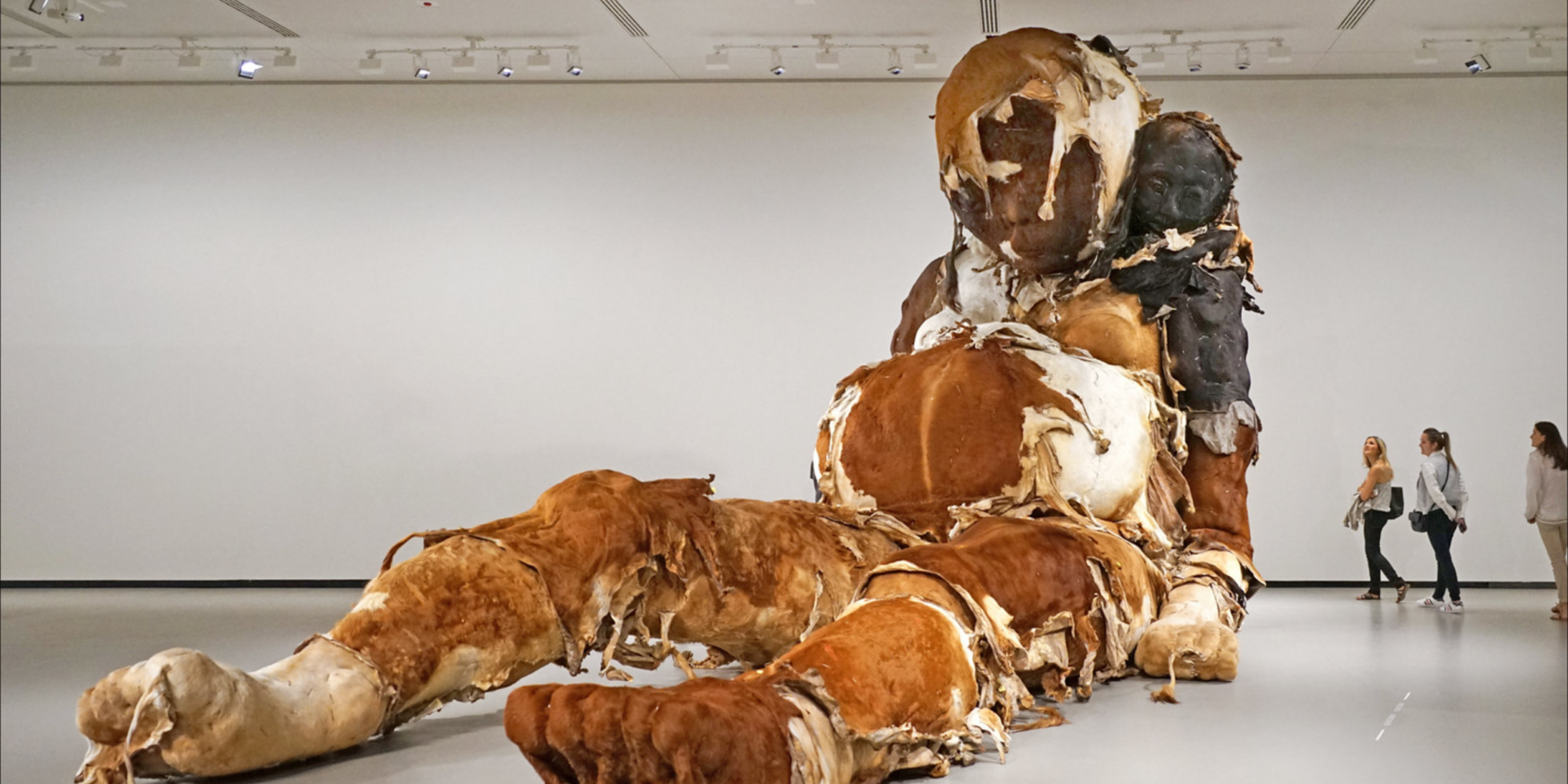 De sculptuur op de afbeelding is "Giant No. 3" van de Chinese kunstenaar Zhang Huan. Het monumentale werk toont een zittende figuur, lijkend op een zwangere bedelaar of een sjamaan, met een kleiner figuur, een zelfportret van de kunstenaar, bij haar nek.